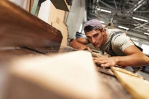 Young carpenter working on woodworking machines in the furniture factory close up